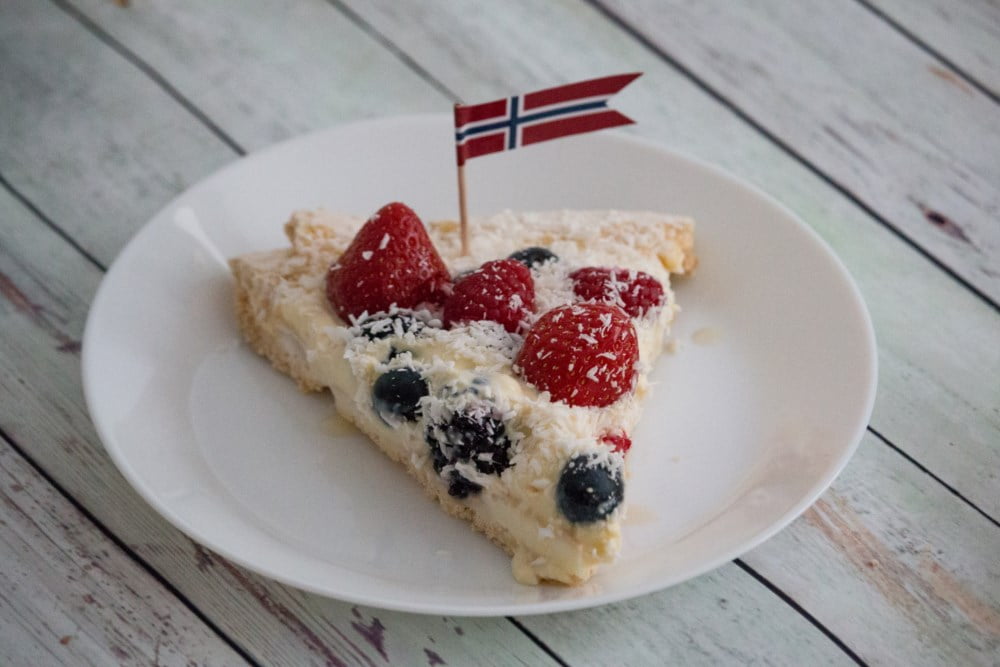 Et kakestykke pyntet med friske bær og et lite norsk flagg på toppen, klart til feiring på 17. mai.