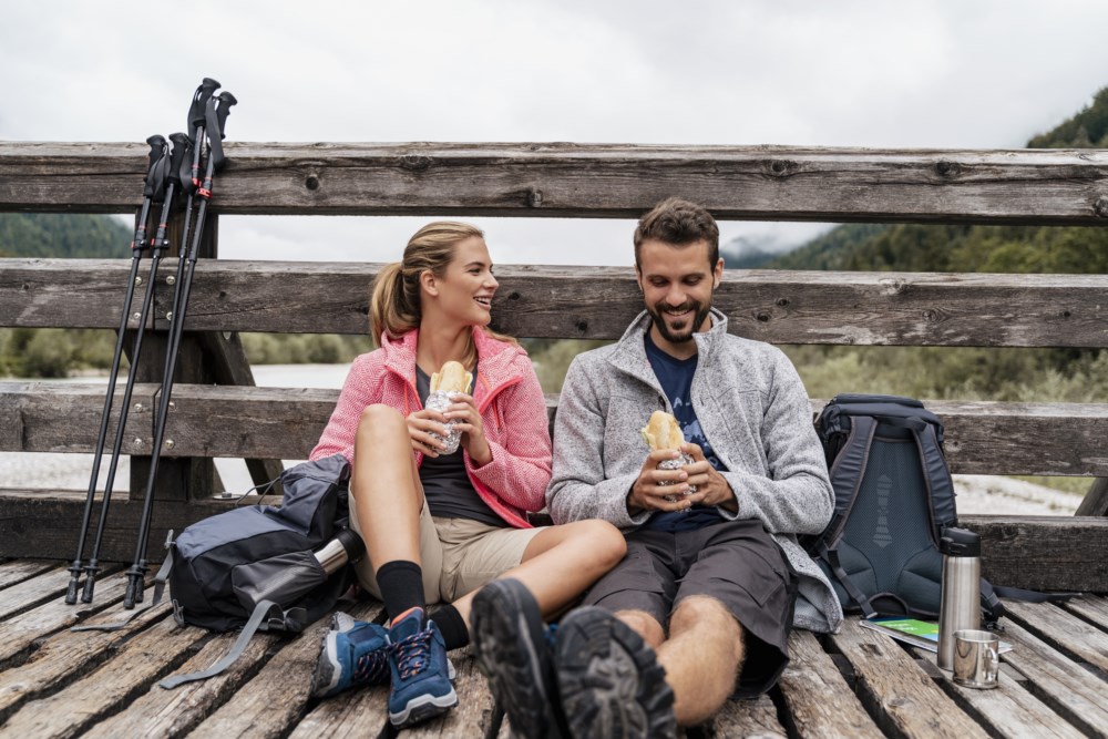 Et ungt par er på tur i fjellet og tar en spisepause på en bro