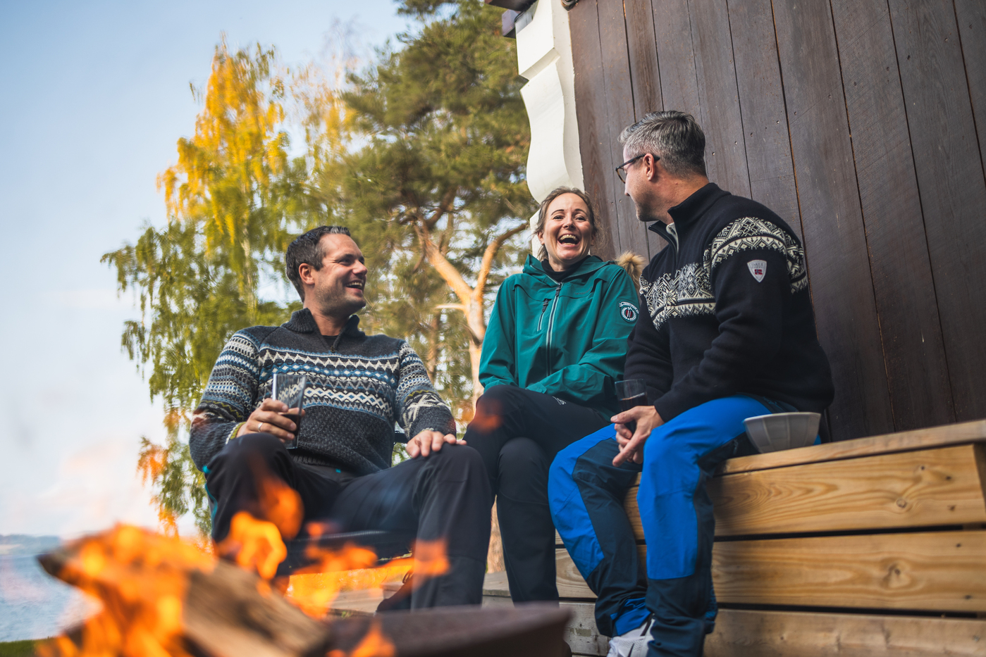 Tre mennesker sitter i hytteveggen foran et bål