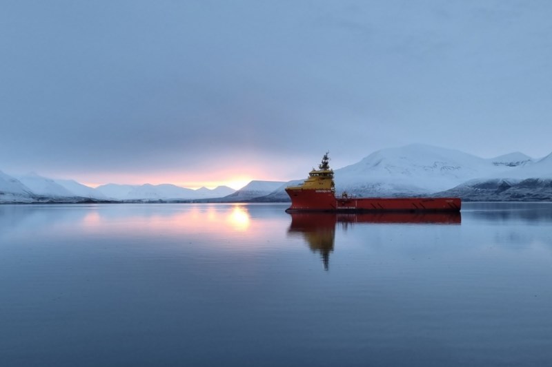 Et skip fra Østensjø Rederi på havet omgitt av vinterkledde fjell i soloppgang