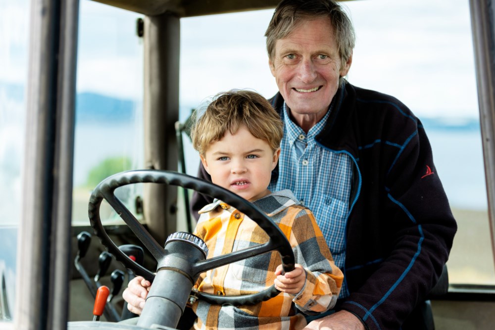 En eldre mann sitter i en traktor med et barnebarn på fanget.