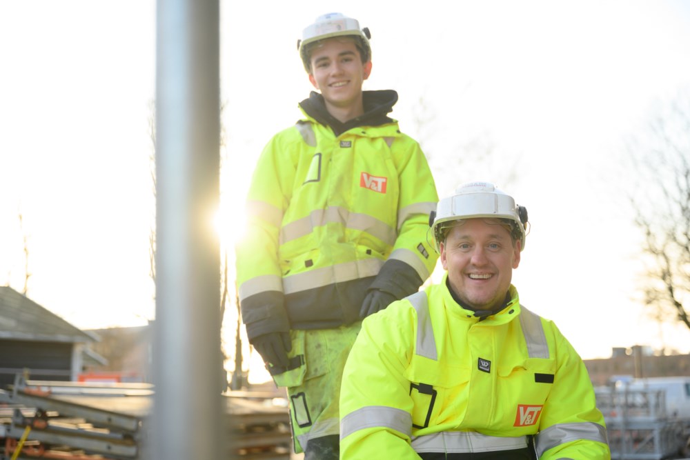 To smilende byggearbeidere i gul dress og hjelm