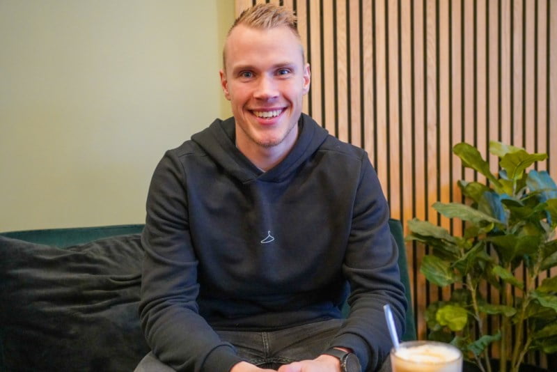 En ung mann med kort lyst hår sitter i sofa og smiler bredt