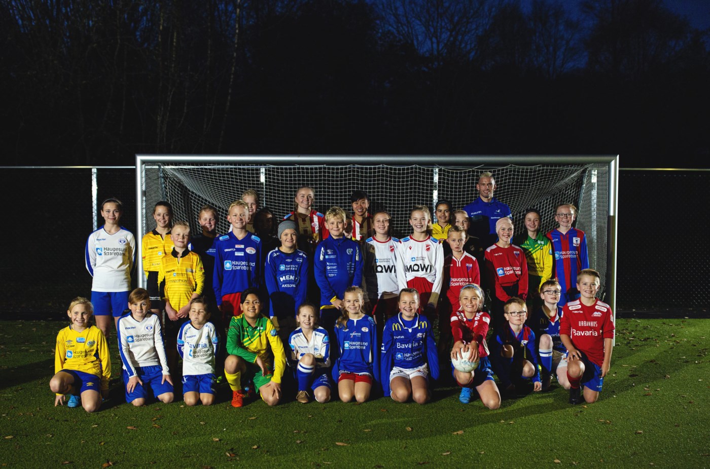 Blide og unge fotballspillere poserer foran et fotballmål