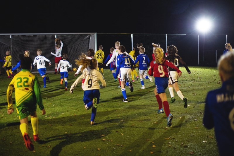Barn i forskjellige fortballdrakter løper på en fotballbane