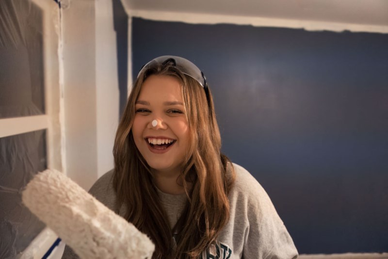 Ung jente maler vegg og har en malingsflekk på nesen