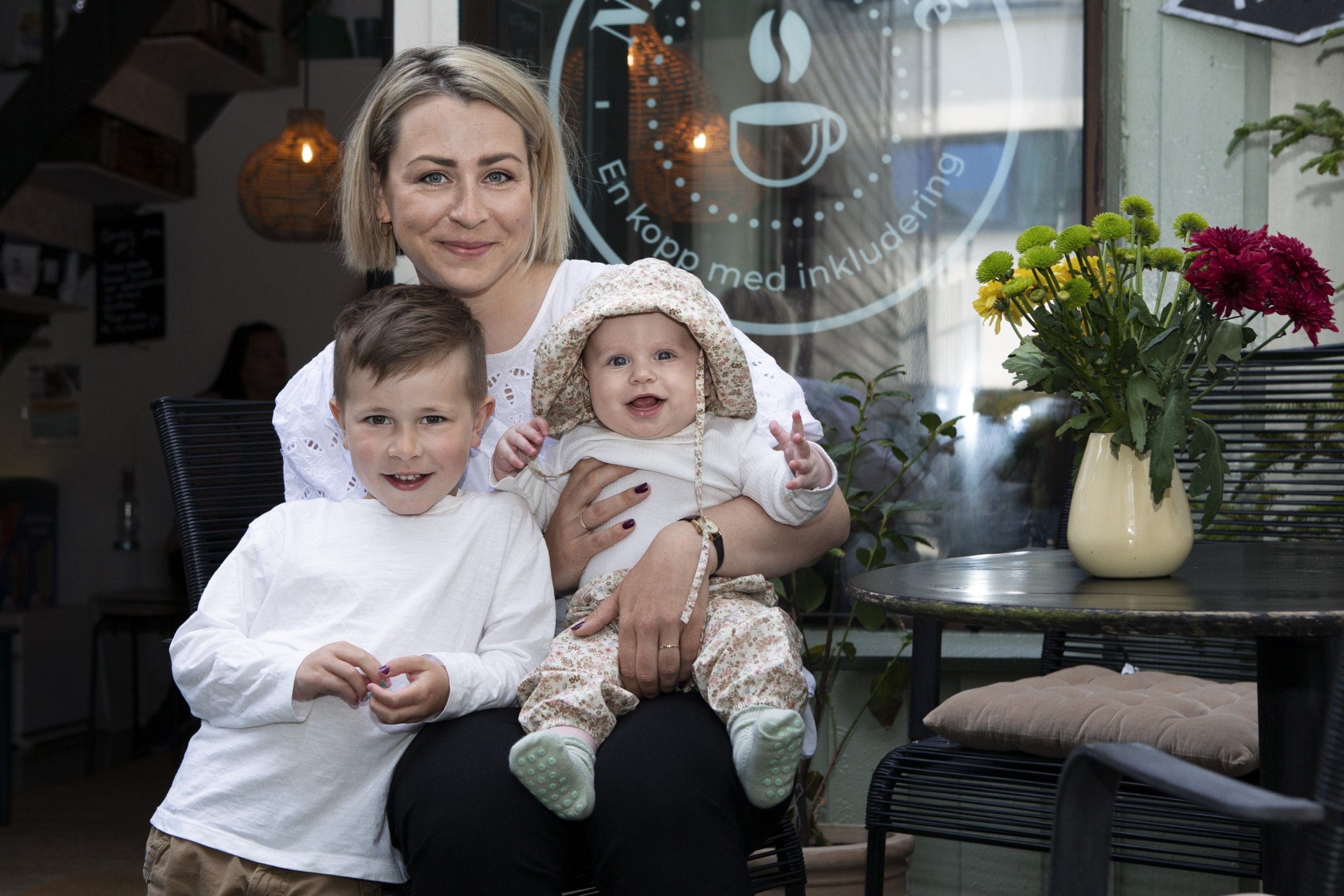 En mor sitter på en kafe med en baby på fanget og en sønn ved siden av seg