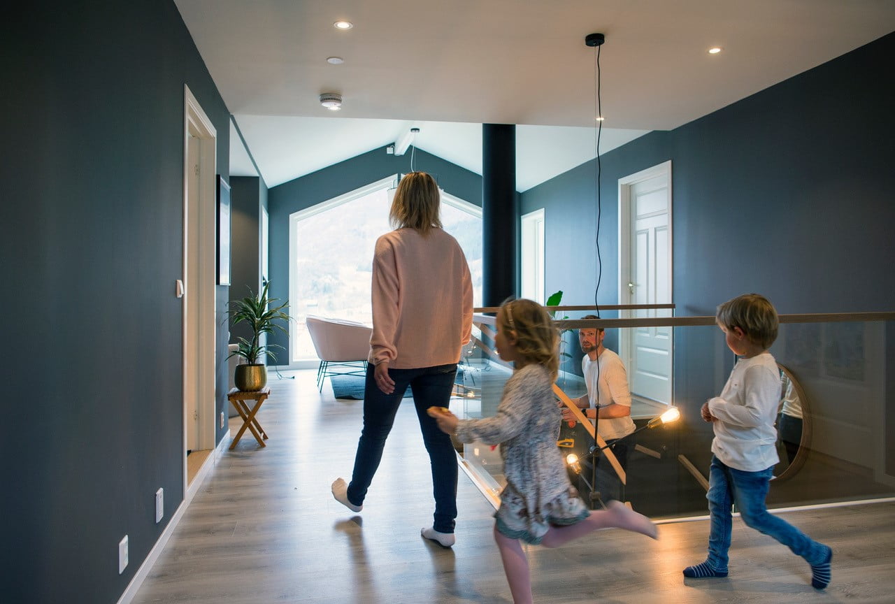 En mann går opp trappen. En dame går mot ham med to unger som løper etter henne