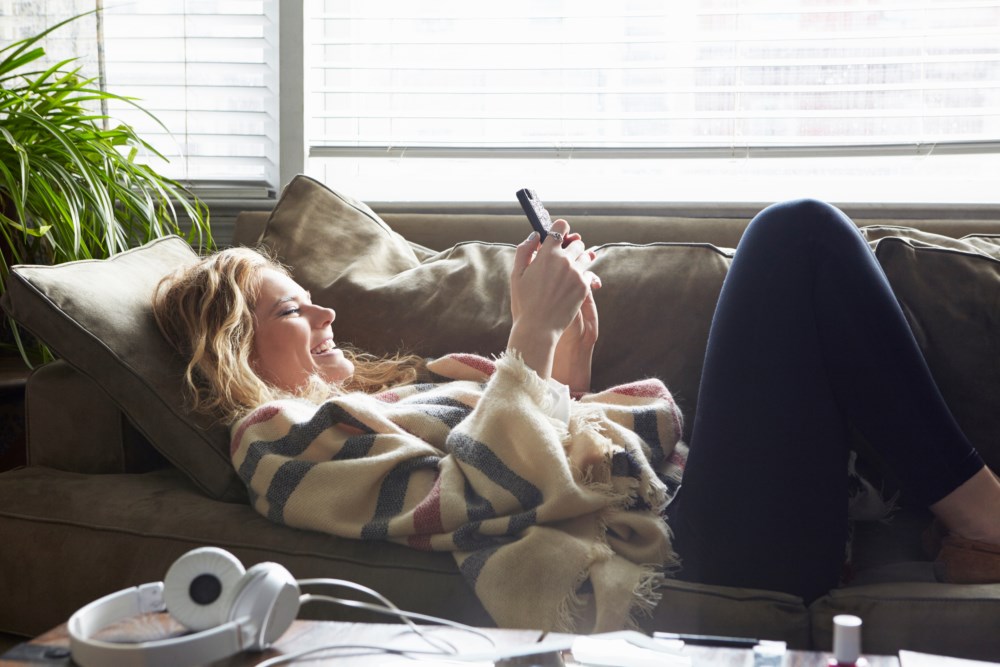 En jente ligger på sofaen og ser på en mobil