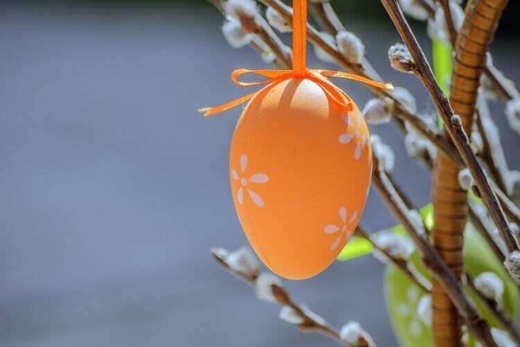 Et oransje påskeegg henger på en gren med