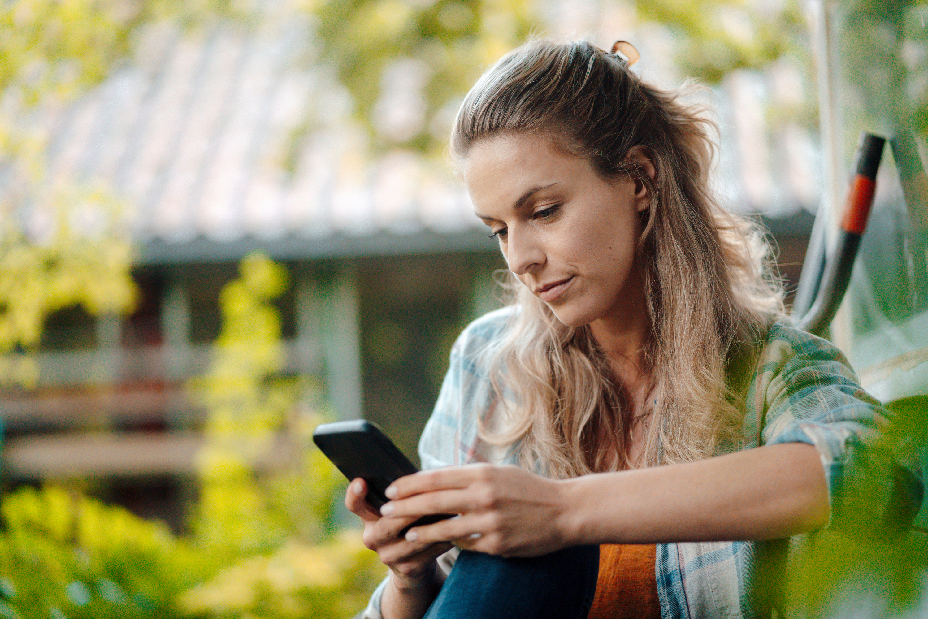 En kvinne ser på mobilen sin mens hun sitter ute i hagen