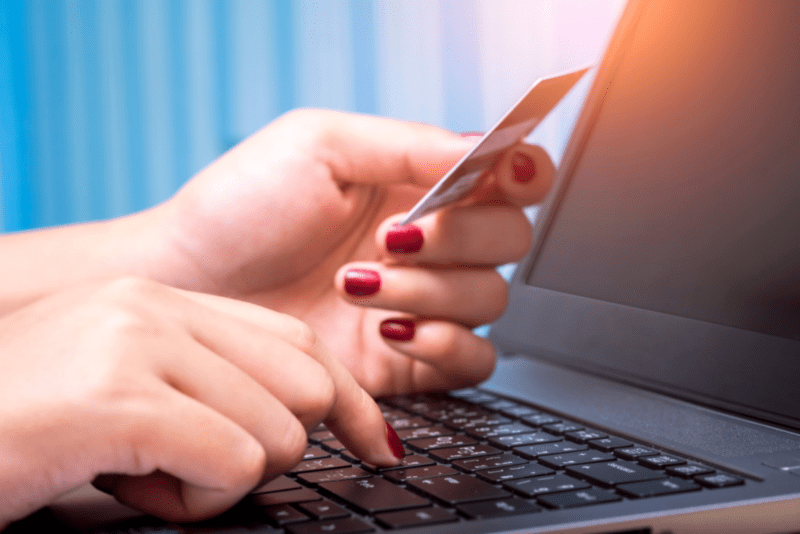 Nærbilde av en kvinne som holder et bankkort og taster på laptopen